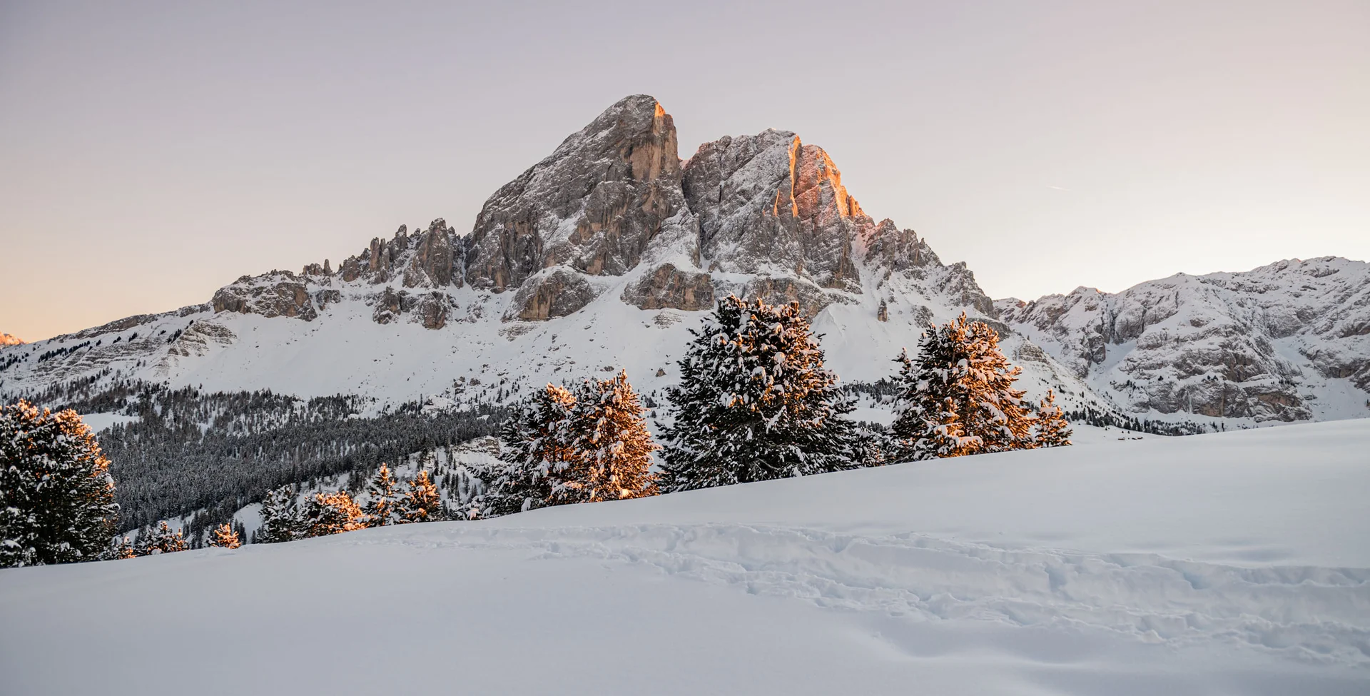 Ihr Chalet in den Dolomiten mit privater Sauna Verschneite Berggipfel und Tannen im warmen Licht der tief stehenden Sonne