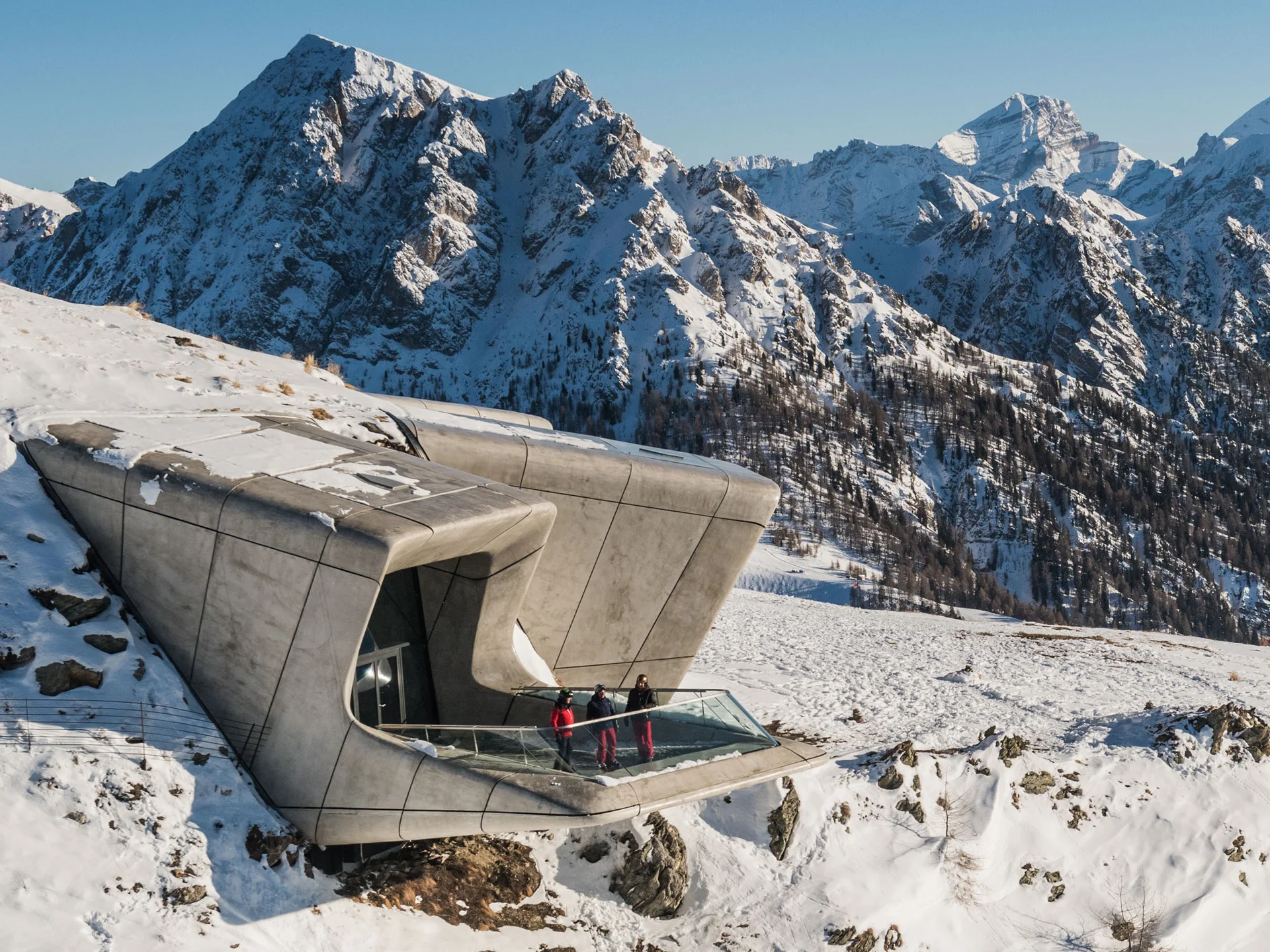 Ihr Chalet in den Dolomiten mit privater Sauna Modernes Gebäude mit Aussichtsplattform in verschneiter Berglandschaft, drei Menschen am Geländer